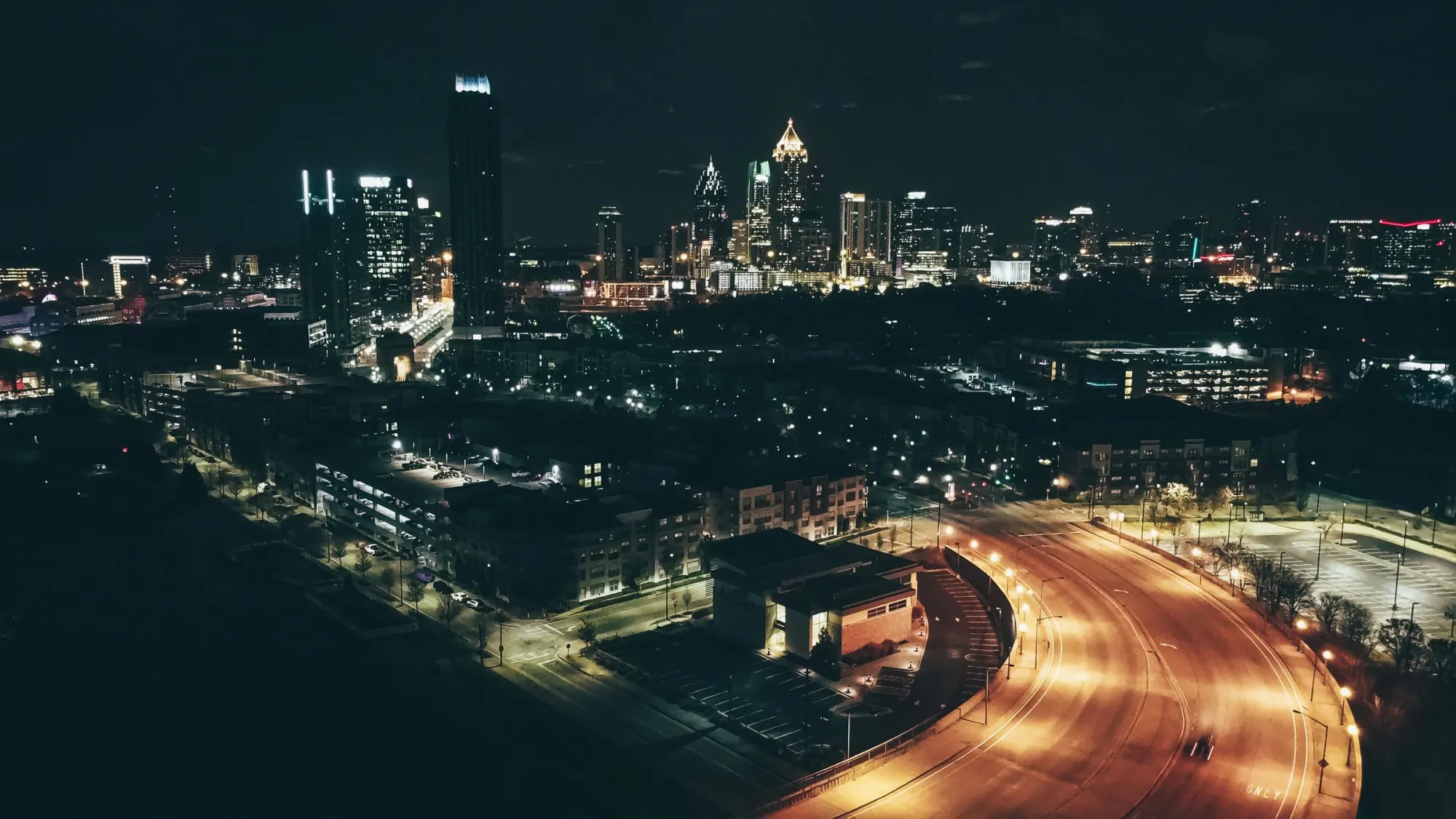 The city at night, seen from the air, with the highway lit below.