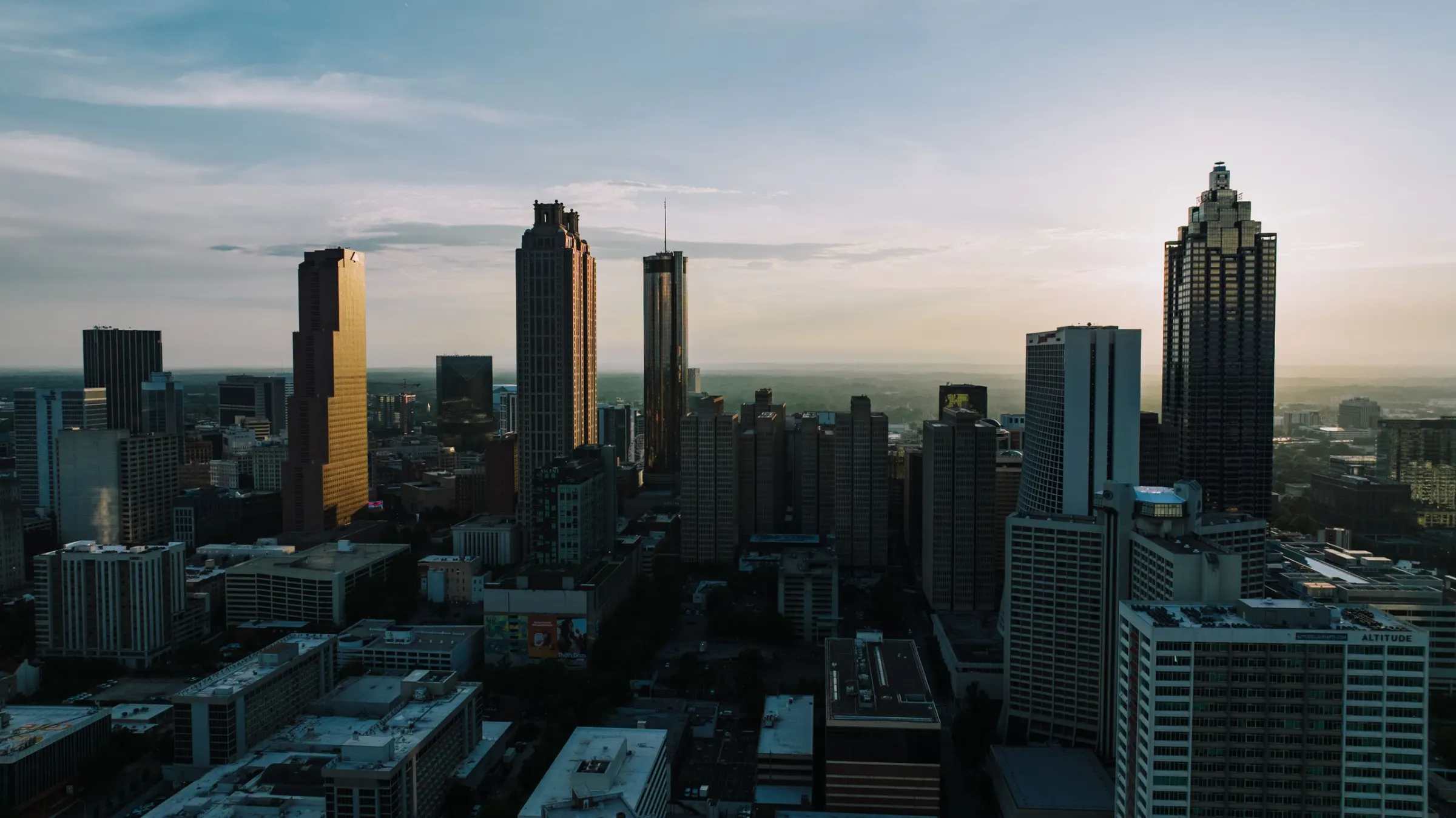 Downtown towers at dusk, seen from the air, with one tower lit gold by the low sun.