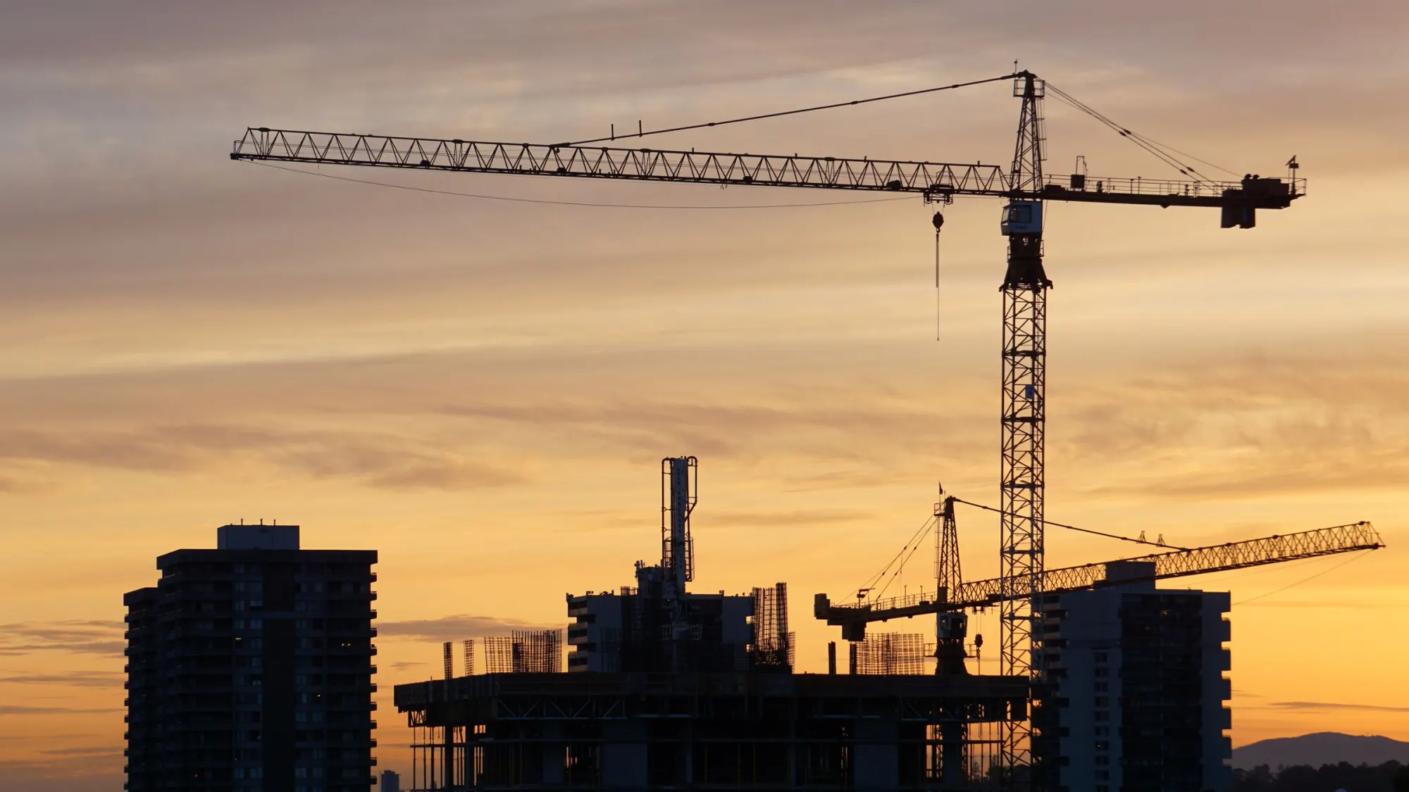 Construction cranes over a building site at sunset.