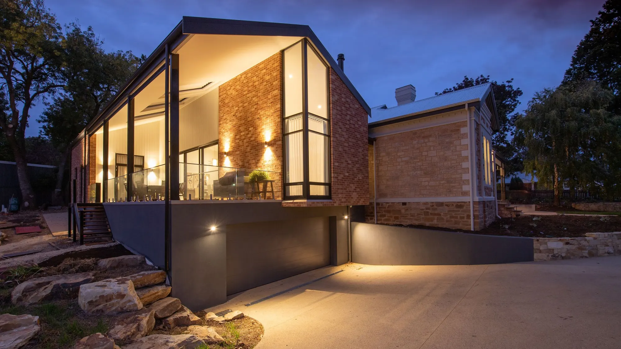 A modern brick house at dusk, with its lights on.