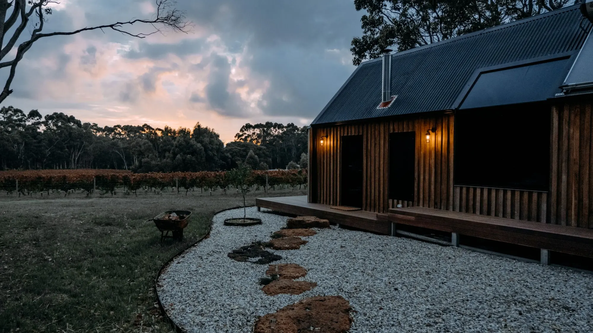 A dark timber cabin at twilight, with a gravel path to the door.