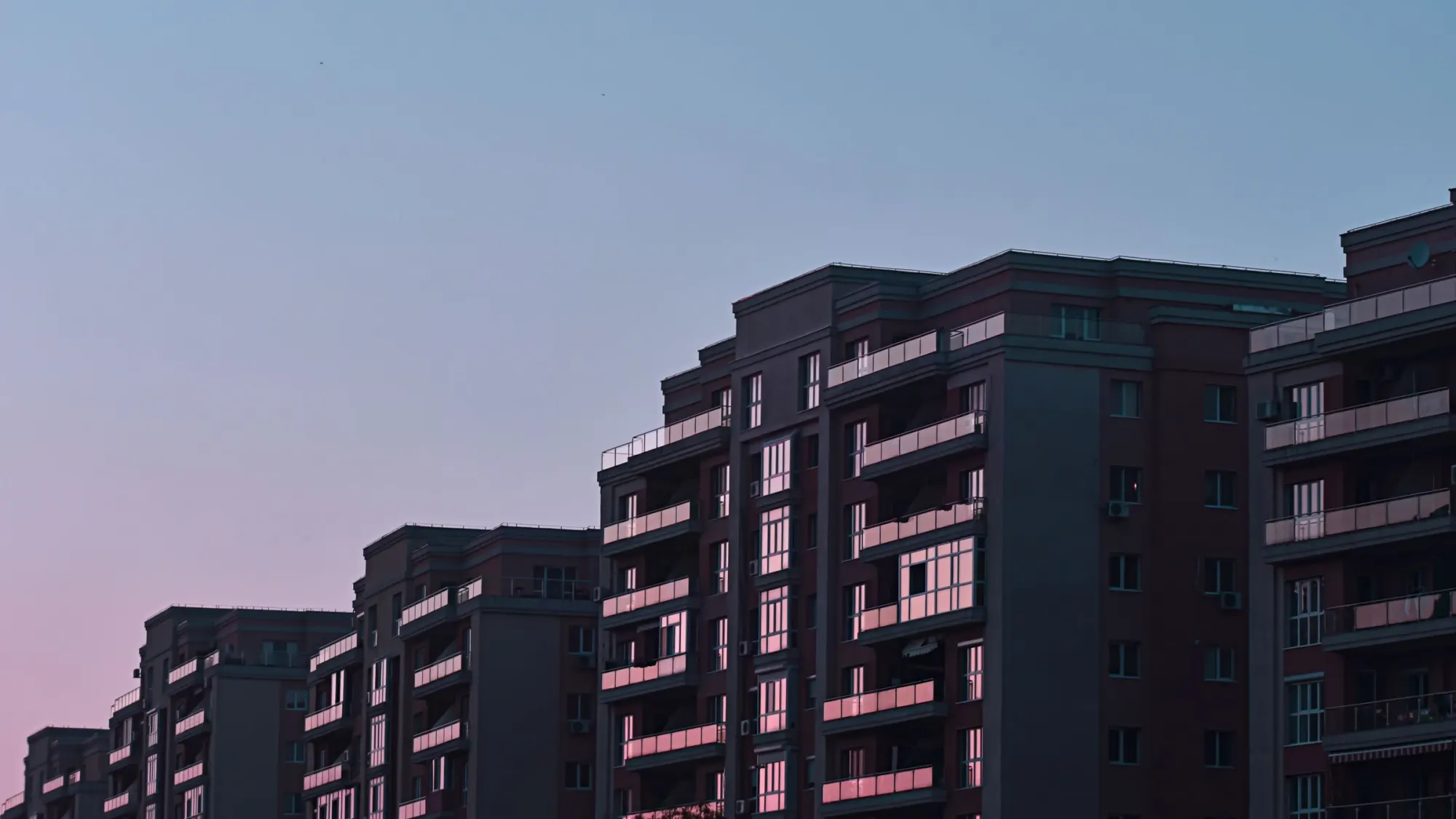 Apartment buildings at dusk, under a pink sky.